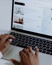 Hands typing on laptop searching Airbnb for accommodation options with map view.